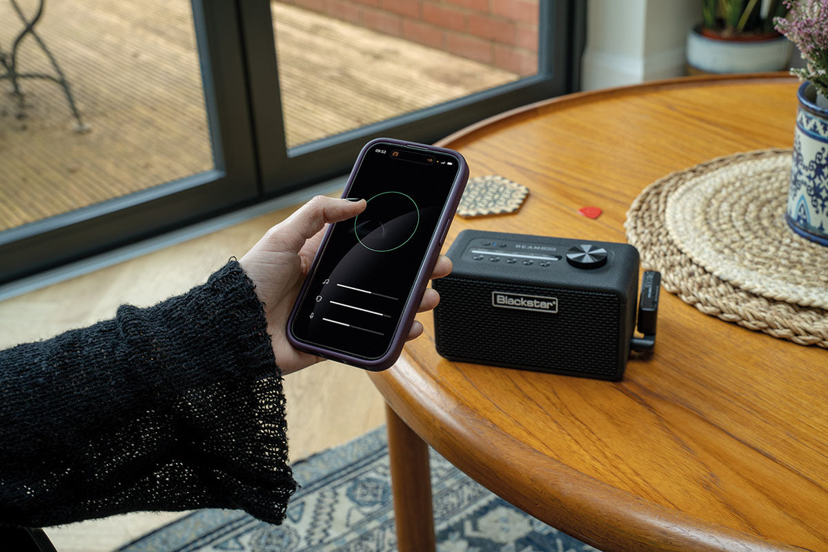 Person using a smartphone with music app next to a BEAM Mini on a wooden table.