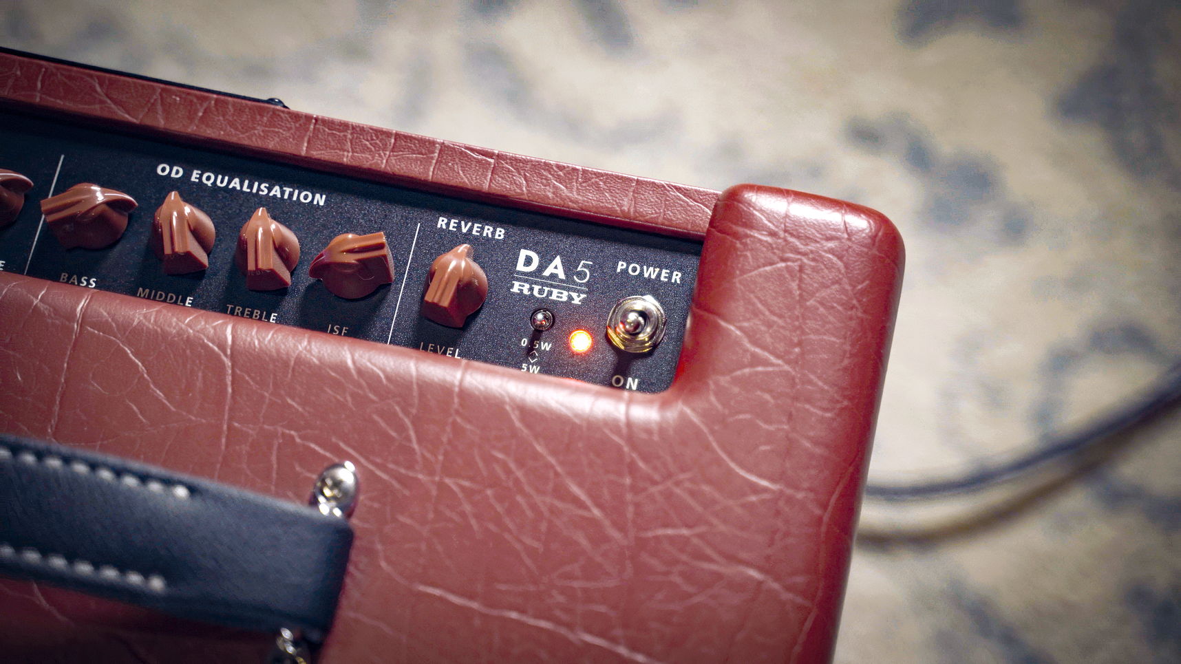 Close-up of a red leather-covered guitar amplifier head with black control panel, knobs, and a visible DA5 RUSH model label.