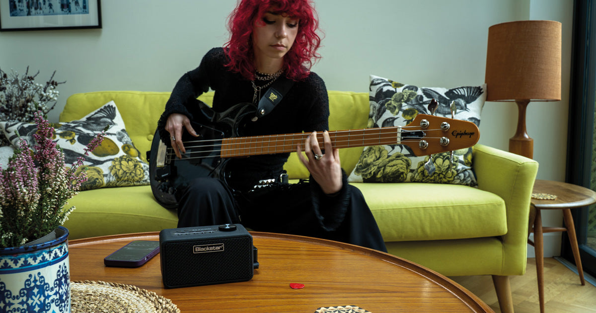 red curly hair playing guitar sitting on a couch with BEAM Mini on a table